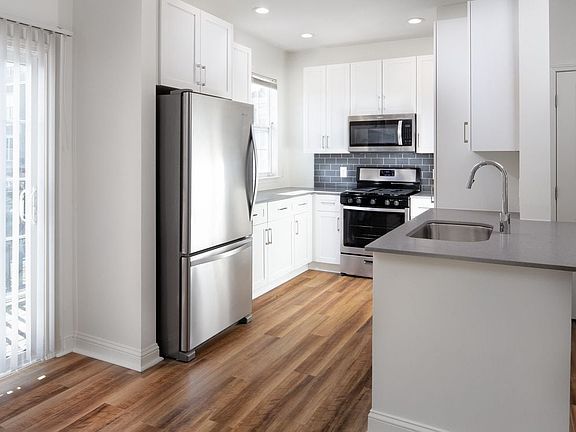 Kitchen with white cabinetry, grey quartz countertops, grey tile backsplash, stainless steel appliances, and hard surface flooring
