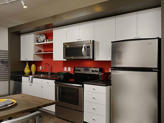 Kitchen with white cabinetry, black countertops, stainless steel appliances and hard surface flooring
