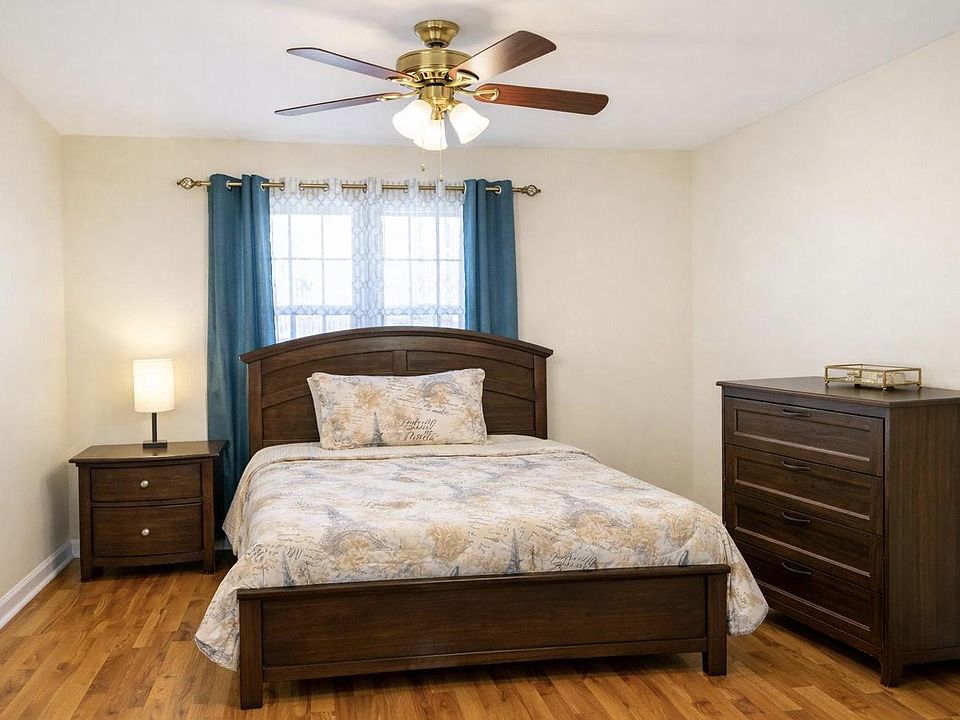 Furnished bedroom featuring a queen bed, matching nightstand and dresser, ceiling fan, and window with curtain panels.