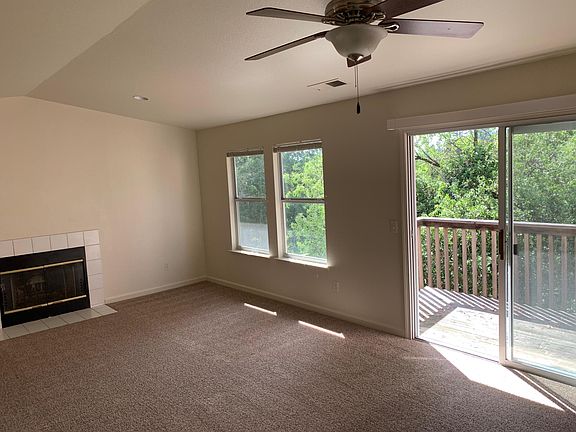 Living room with fireplace, ceiling fan, and deck balcony.