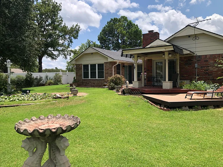 Rear view of house. Pond on the left, sunroom in the middle and master bedroom door and deck on the right.