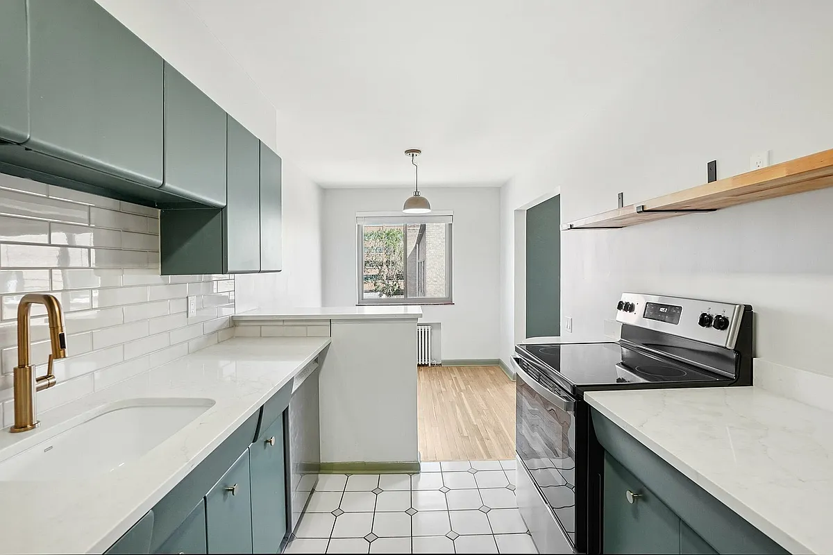 Modern kitchen with sleek white countertops, stylish green cabinetry, and stainless steel appliances, featuring elegant subway tile backsplash and natural light from the large window. - Lucca Apartments