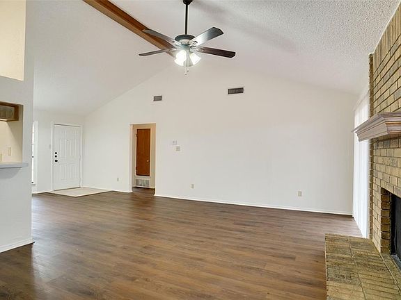 Unfurnished living room featuring high vaulted ceiling, a brick fireplace, ceiling fan, a textured ceiling, and dark hardwood / wood-style flooring
