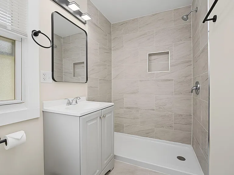 Updated bathroom with tiled walk-in shower, built-in niche shelving, and vanity storage with modern mirror lighting.