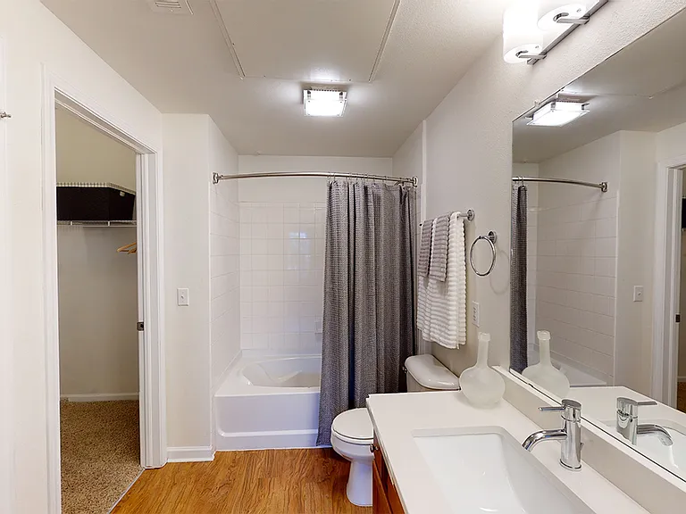 Apartment bathroom with wood-style flooring. Quartz-style countertops (shown here) are available in select homes.