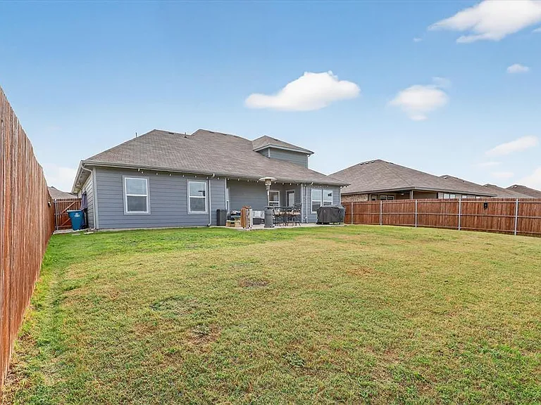 Expansive backyard featuring a lush lawn, privacy fencing, and a concrete patio