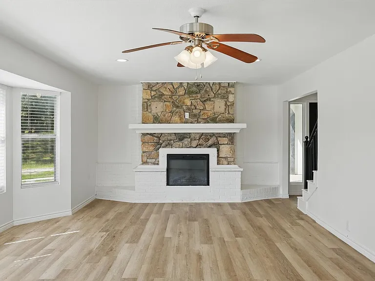 Unfurnished living room featuring light wood finished floors, stairway, ceiling fan, a stone fireplace, and baseboards