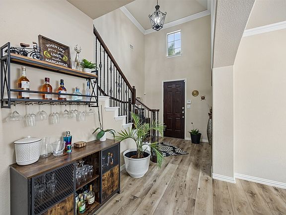 Two-story foyer with a dark wood-finish entry door, wood-finish flooring, and crown molding