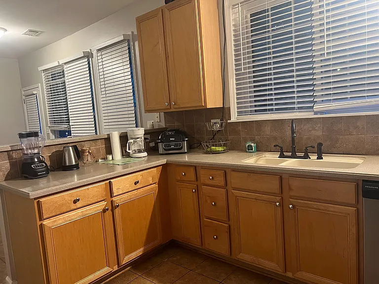 Spacious kitchen workspace with ample wood cabinetry, generous counters, tiled backsplash, and a sink set beneath wide window