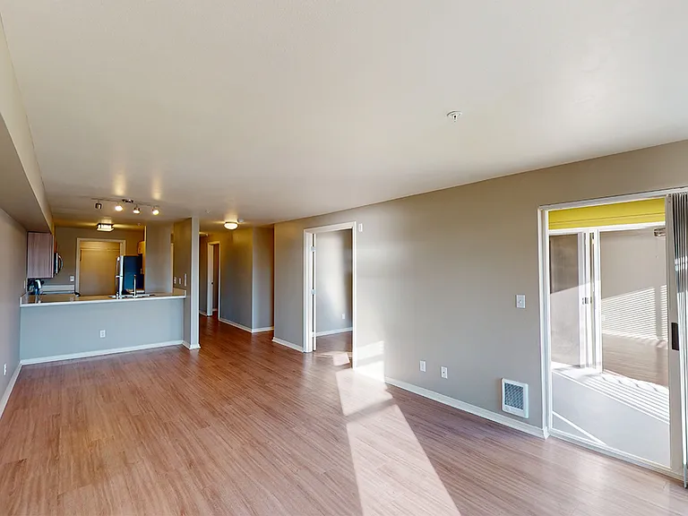 Apartment kitchen with stainless steel appliances, dining and living room with wood-style flooring.