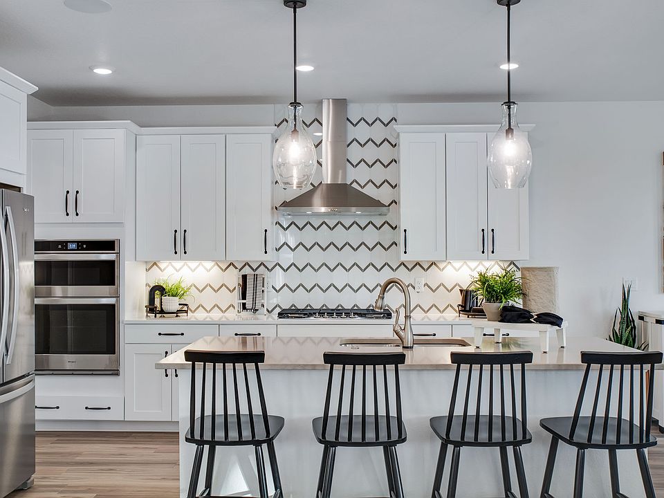 A modern, well-designed kitchen with white cabinets, a patterned backsplash, and pendant lights over