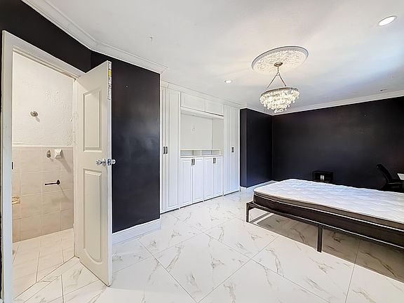 Spacious bedroom with built-in cabinetry, tile flooring, and chandelier lighting, plus an ensuite bath access.