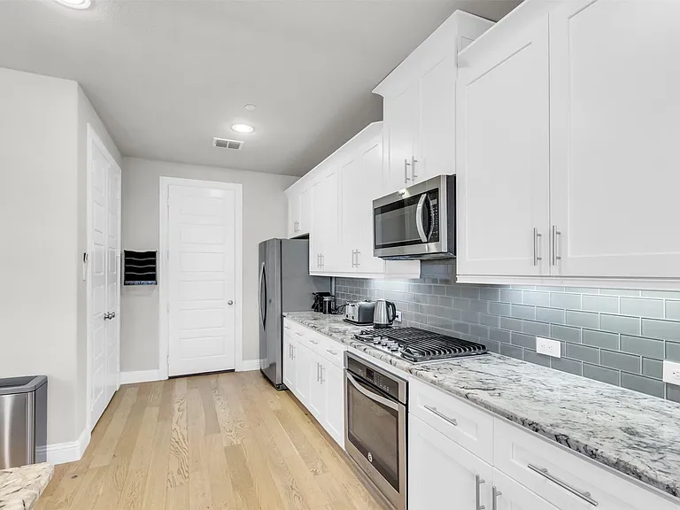 Kitchen featuring white shaker cabinetry, stainless steel appliances, light-toned wood-finish flooring, a gas range, and a subway tile backsplash