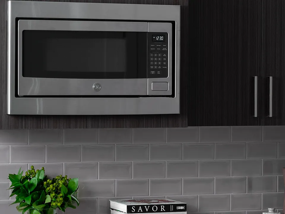 Elegant kitchen featuring sleek GE stainless steel microwave, modern slow close dark wood cabinetry, and stylish subway tile backsplash.