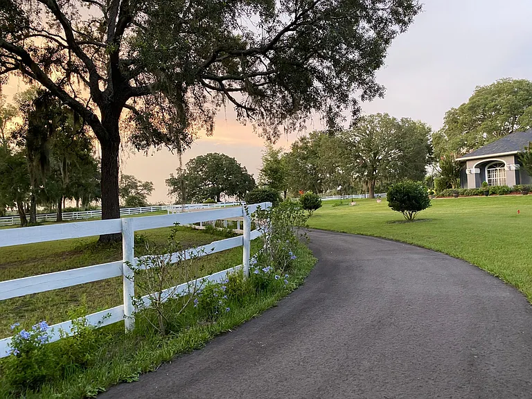Driveway leads to house. The horse fencing has 4 boards all around the outside of the property and 3 on the inside. All fencing is white.
