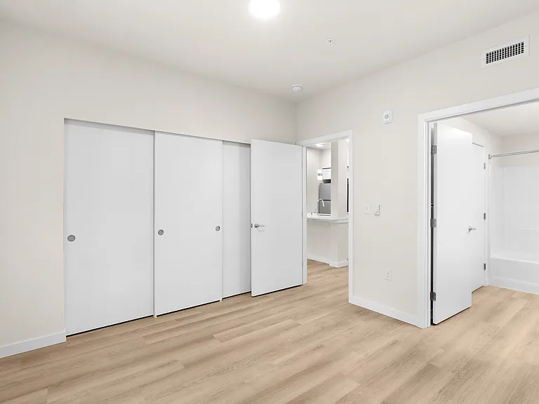 Sun-lit apartment bedroom featuring wood-style floors and sliding closet storage. Sun-lit apartment bedroom featuring wood-style floors and sliding closet storage.