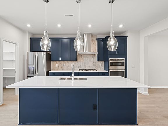 A modern, open-concept kitchen with a large white island, navy blue cabinets, and pendant lighting f