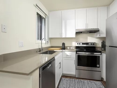 Renovated I kitchen with grey quartz countertops, white cabinetry, stainless steel appliances, and hard surface flooring - eaves Warner Center