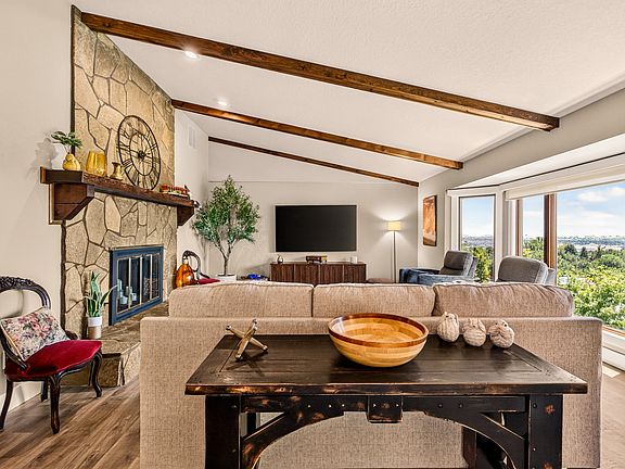 The spacious main living room features vaulted ceilings, exposed wood beams, a stone fireplace, and panoramic Treasure Valley views. Comfortable seating, abundant natural light, and a 75" TV create the perfect space to relax, connect, or unwind.
