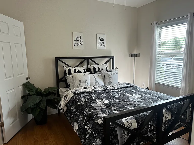 Charming bedroom with chic black and white decor, modern metal bedframe, and abundant natural light from a large window. Charming bedroom with chic black and white decor, modern metal bedframe, and abundant natural light from a large window.
