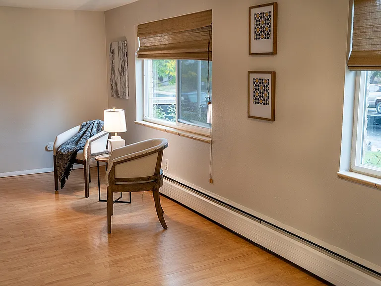 Cozy and elegant corner nook featuring soft armchairs, a warm table lamp, and large windows with chic blinds, creating a serene atmosphere.