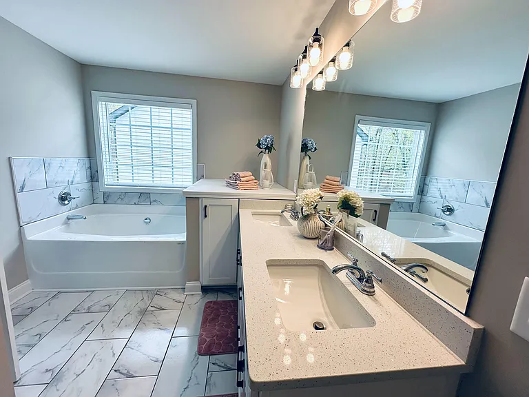 Spacious bathroom with dual-sink vanity, large mirror, soaking tub, and tile floors, plus a window for added light.