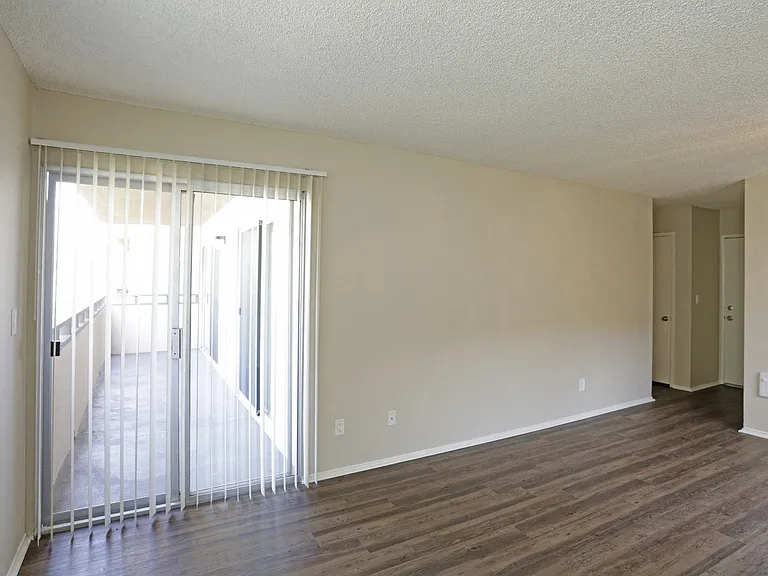 Living room with plank style flooring and sliding glass doors to private porch at Villa Pacific Apartments in Oceanside, California.