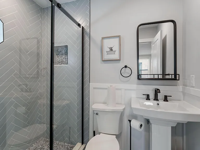 Clean bathroom with glass-enclosed shower, patterned tile surround, and pedestal sink with wall mirror and matte-black fixtur