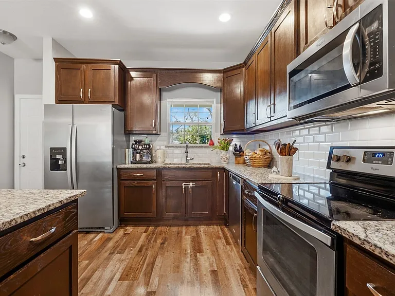 Kitchen featuring dark wood cabinetry, stainless steel appliances, light granite countertops, white subway tile backsplash, and wood-finish flooring