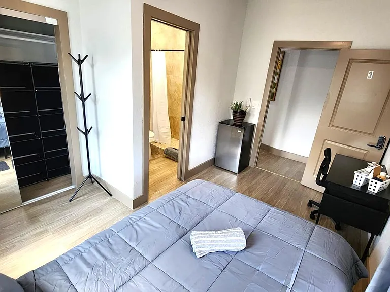 Furnished bedroom with a full bed, desk/work area, and mirrored wardrobe; convenient access to the bathroom nearby.