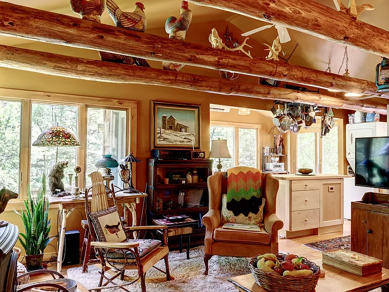 Beamed Living Area with country furniture, flat screen TV on primitive cabinet with kitchen island and pot rack with Dining Area in the distance.
