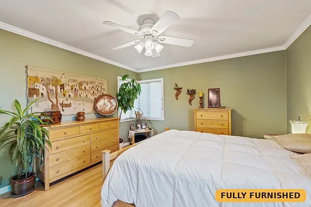 Large bedroom on the main level with 3 windows, a queen bed, ceiling fan, reading chair, two dressers and a large closet with sliding mirrored doors.