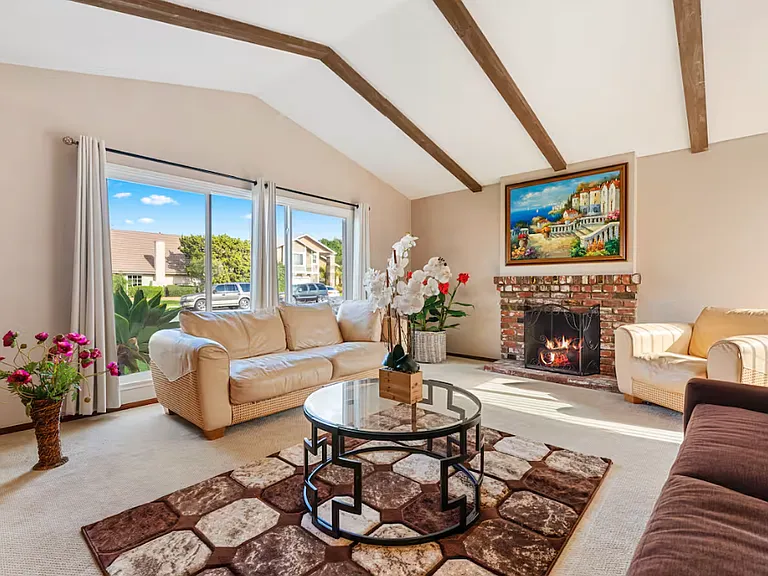 This carpeted living room has a fireplace and the view of the quiet spacious residential street.