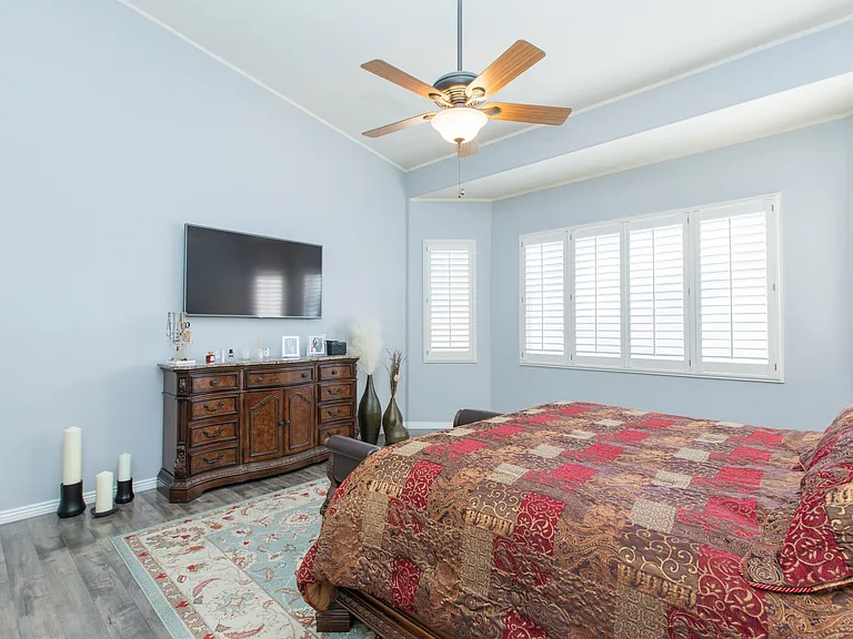 Very spacious primary suite or master bedroom featuring vintage oak wood-look flooring, vaulted ceilings & window wood shutters
