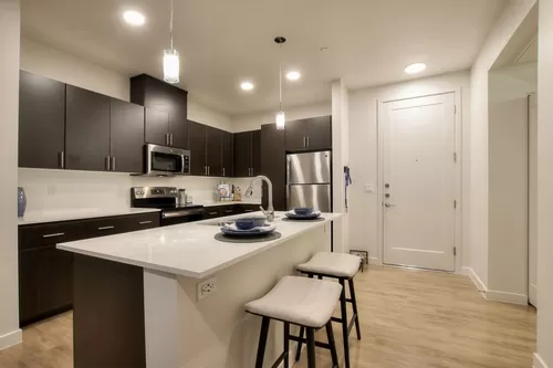 Large kitchen with kitchen island, modern lighting, quartz counters, and espresso slab cabinets. - View 32 Apartments