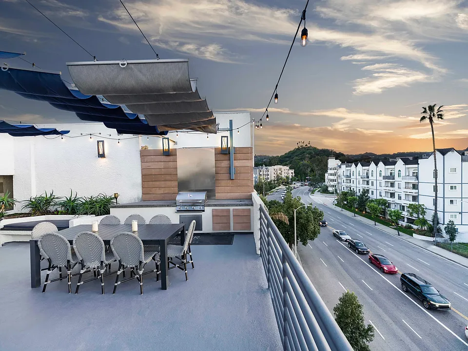 Rooftop lounge with outdoor dining, grilling area, and sunset views over Sherman Oaks.