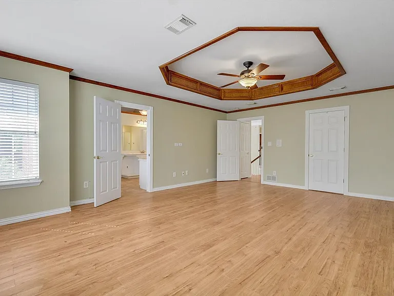 2nd Story Primary Bedroom featuring wood flooring, a tray ceiling with wood-paneled trim, a ceiling fan, and private ensuite and two closets.