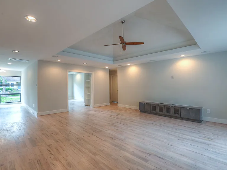 Living room view of tray ceiling, designer ceiling fan, picture window in foyer facing the street, built-in media credenza, and opening to flex room/office