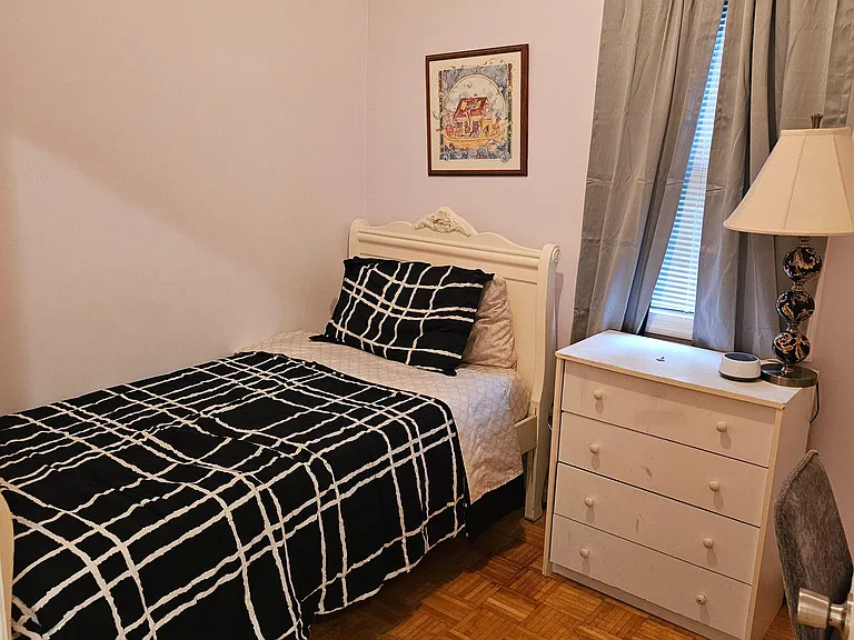 Furnished bedroom with a twin bed, dresser, and nightstand, plus a window with curtains for light and privacy.