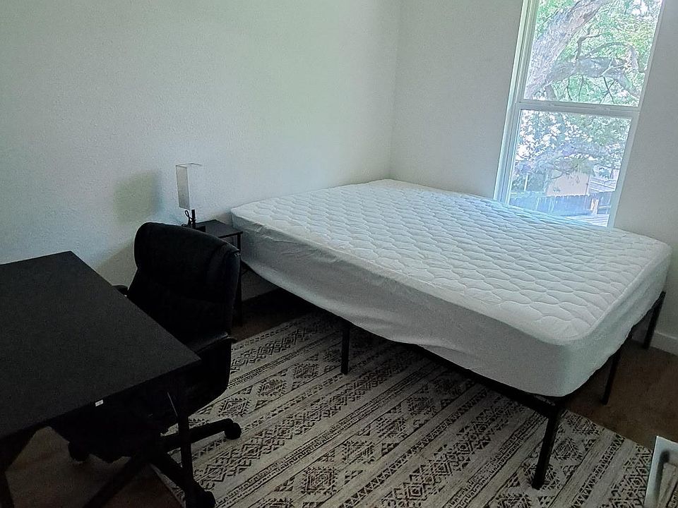 Private bedroom with a large window, twin bed, side table with lamp, and a dedicated desk area for work or study.