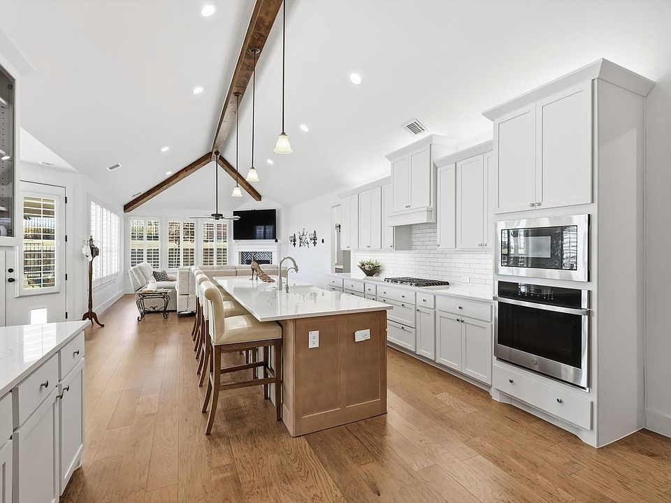 Stunning great room with high ceilings and a fireplace!  Notice the wood beamed ceilings and natural light. The kitchen includes white cabinets, designer backsplash, appliances with stainless steel finishes, open floor plan, and pendant lighting.