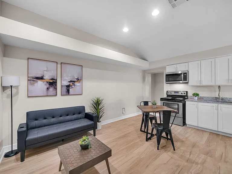 Open-concept living area with seating and a dining nook, flowing into a kitchen with white cabinetry and stainless appliances