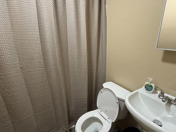 Full bathroom with tub/shower combo, textured shower curtain, and a compact vanity with sink and mirror.