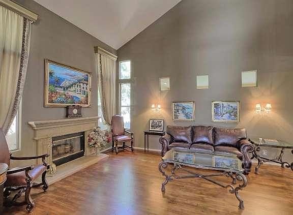Shiny wood flooring sets the tone for the formal living room with soaring ceiling and elegant fireplace