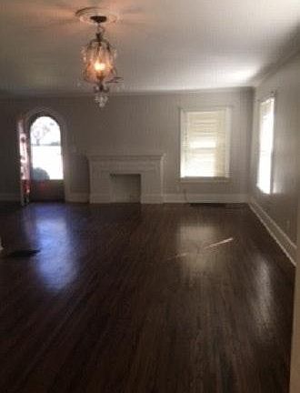 Living room with open dining area. All windows have wooden slat blinds. Fake fireplace, extra space to side for open entry area.