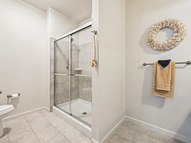 Modern bathroom with elegant glass shower, neutral tile flooring, and decorative floral wall accent.