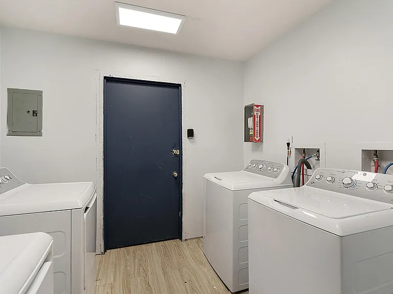 Modern laundry room with two sleek, white washing machines, bright lighting, and a stylish dark door.
