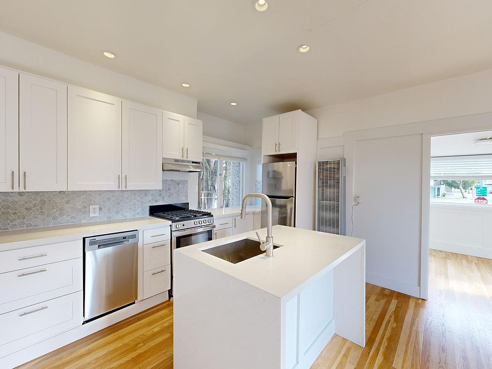 Kitchen with multiple cabinets, refrigerator, stove, range hood, and sink
