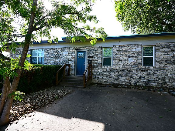 Stone exterior with two off street parking spaces and trees.