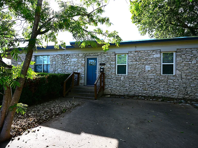 Stone exterior with two off street parking spaces and trees.
